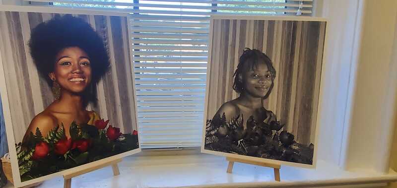 Two portraits of Black women, one in color and one in B/W on easels. 