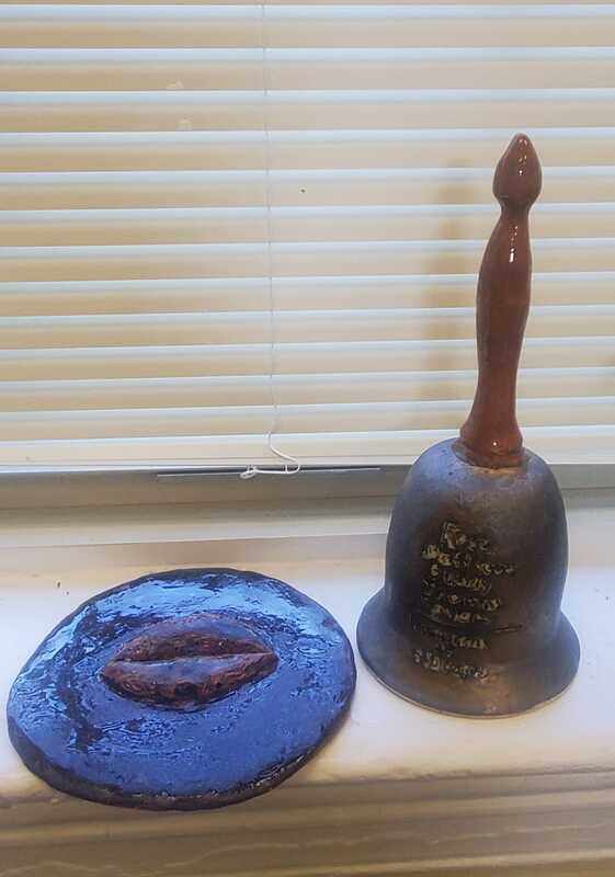 Close up a ceramic bell with names written on front and a clapper featuring a pair of lips. 