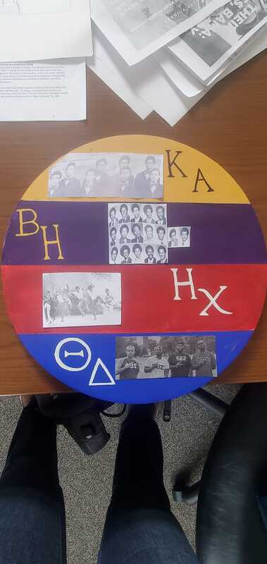 Close up a striped wooden circle with yearbook images and handwritten Greek symbols on it. 