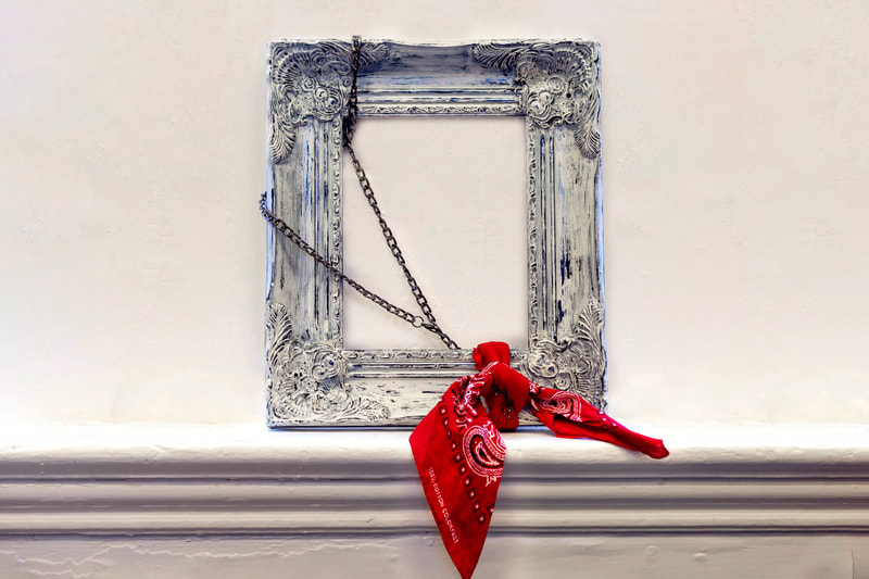 Distressed wood frame with a small chain wrapped around the edge and a red bandana tied in the lower right corner. 