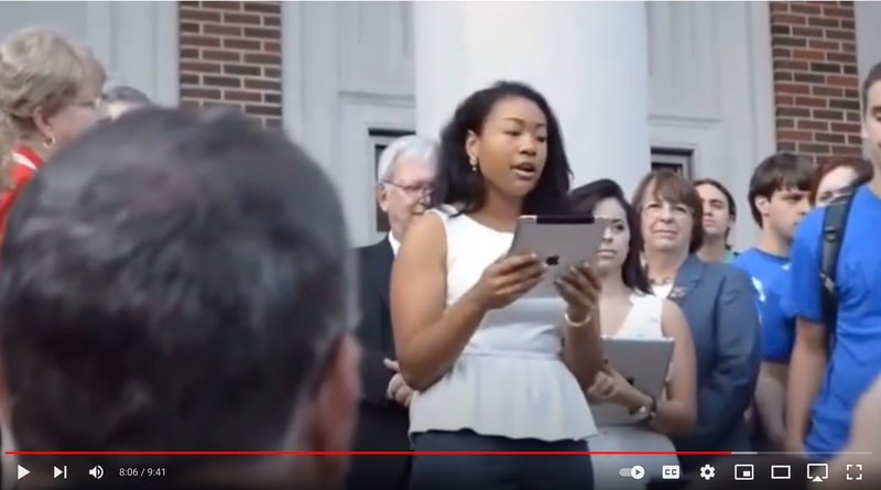 Film still of a Black woman reading demands at a campus protest demanding desegregation of the UA sororities. 